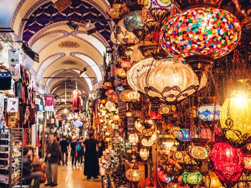 A vibrant market corridor filled with colorful mosaic lanterns hanging from the ceiling.