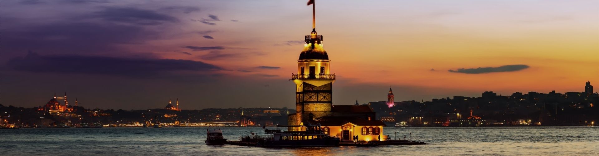 A tower illuminated at sunset stands on a small islet in the water.
