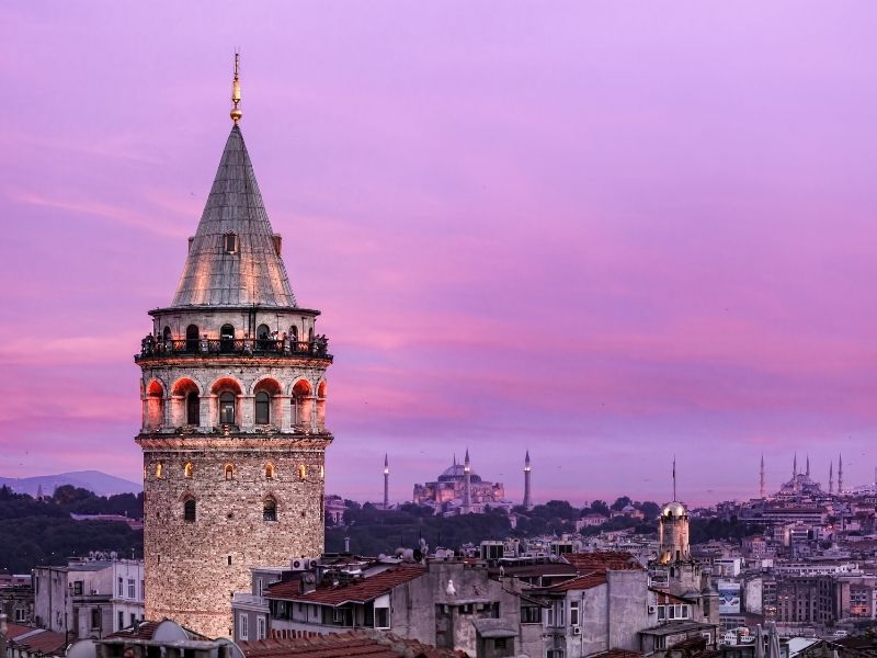 The Galata Tower stands tall against a vibrant pink and purple sunset sky in Istanbul.
