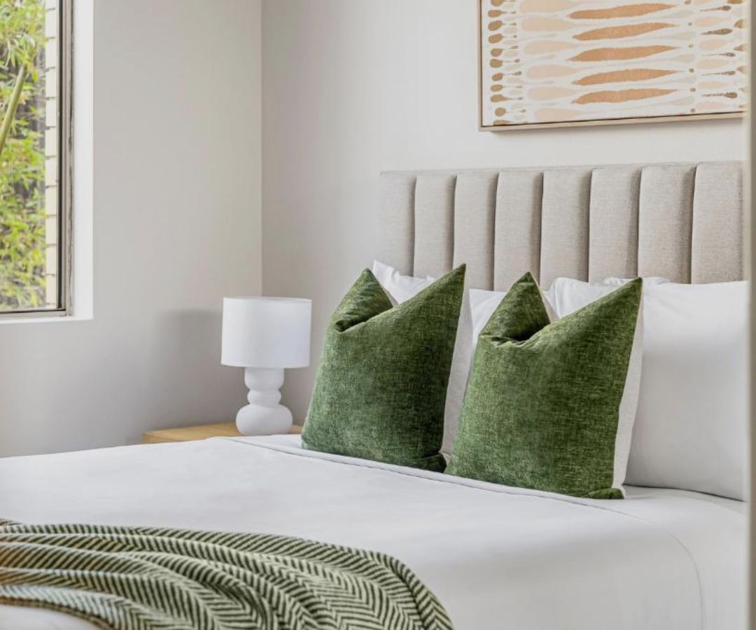 Neatly made hotel bed with green pillows