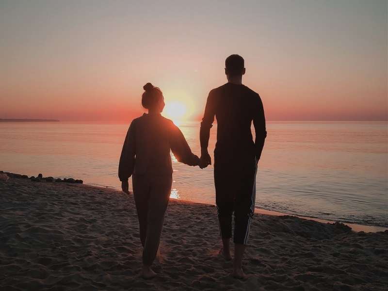 couple walking holding hands at sunset in beach