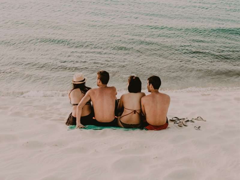 friends sitting on beach watching waves