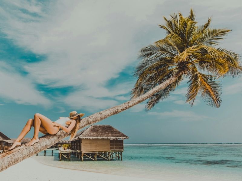 lady relaxing on palm tree with overwater bungalow in background