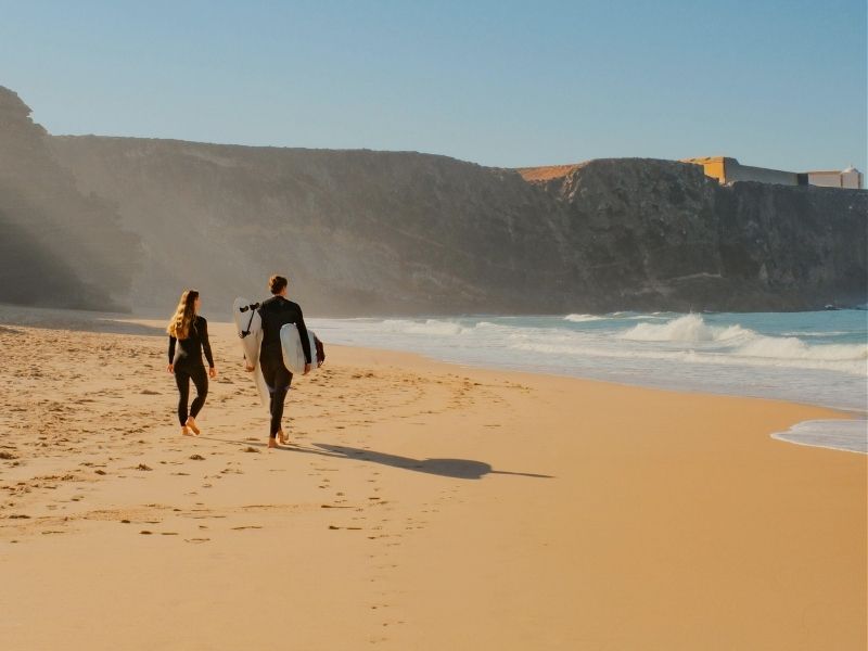 couple walking along the beach with surf boards