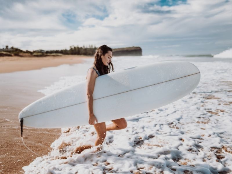 women with surboard walking into ocean