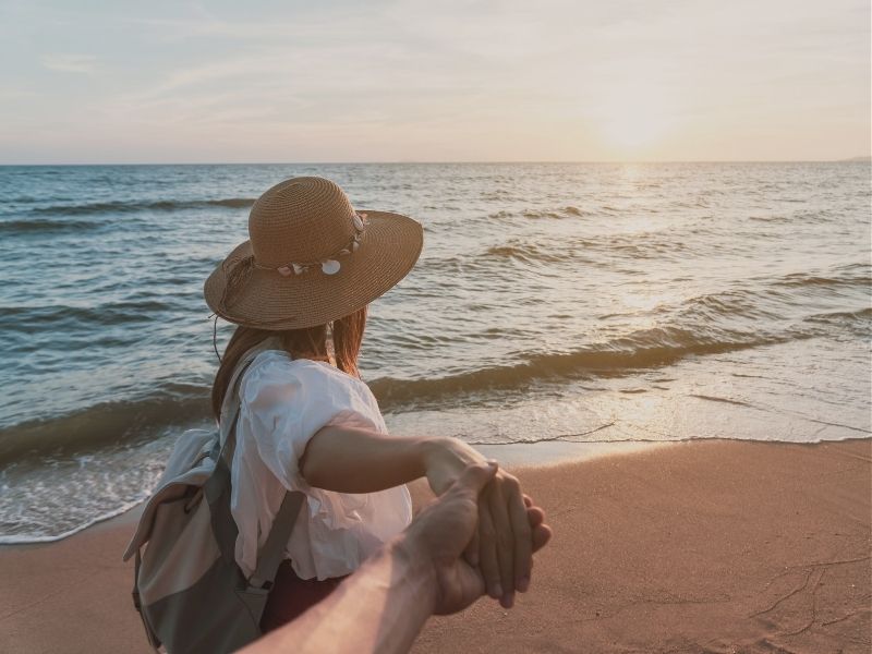 woman holding hands while standing on beach at sunset