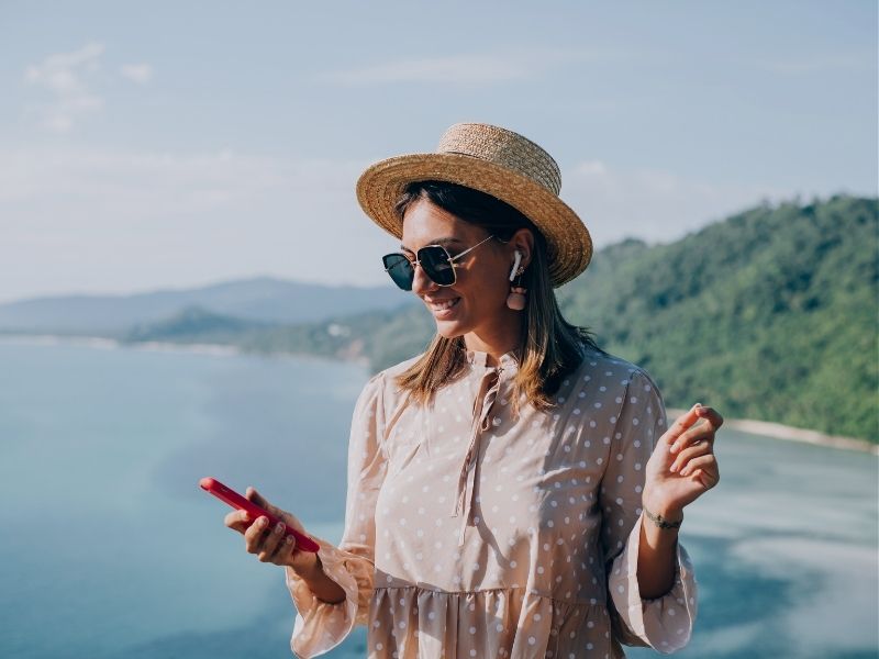 young woman in summer dress and straw-hat sunglasses dancing with smartphone in hand listening to music